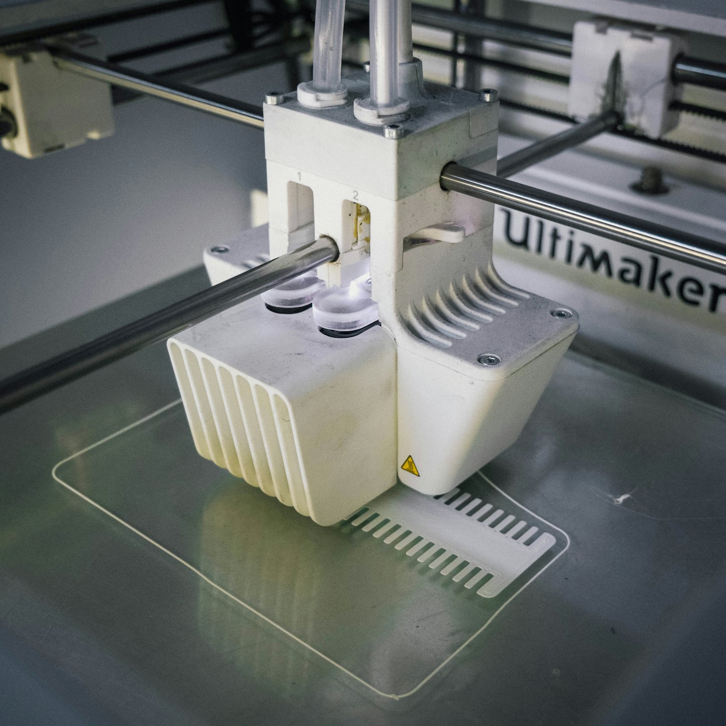 3D printer extruding white filament onto a metallic bed.