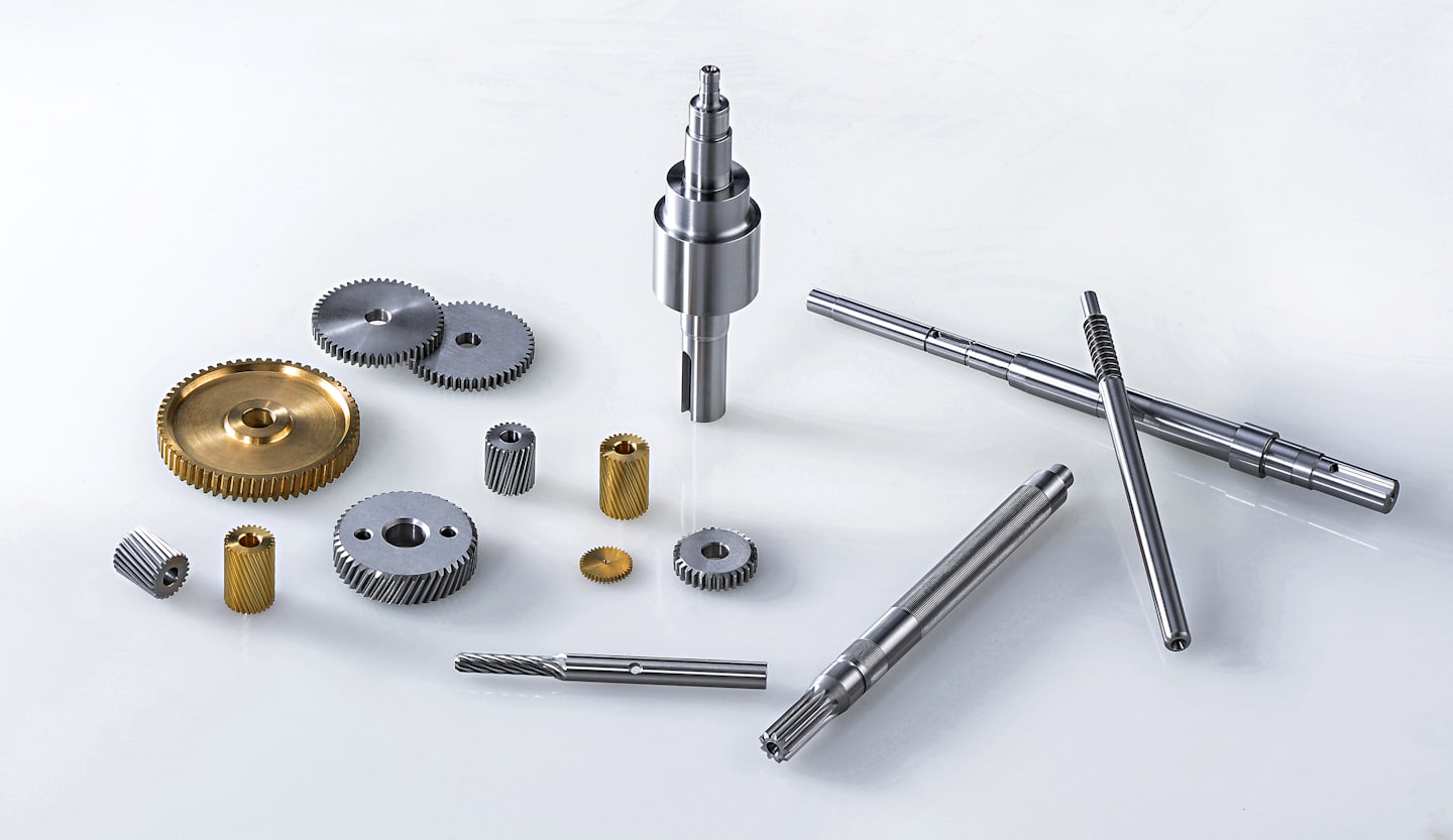 Assorted metal gears and shafts arranged on a white surface.
