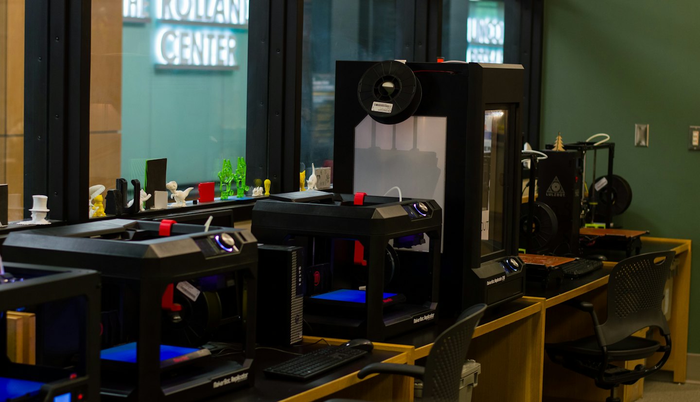 Multiple 3D printers with colorful models on a shelf.